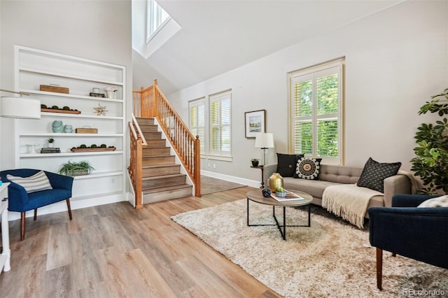 living room featuring light hardwood / wood-style floors, built in shelves, a wealth of natural light, and high vaulted ceiling