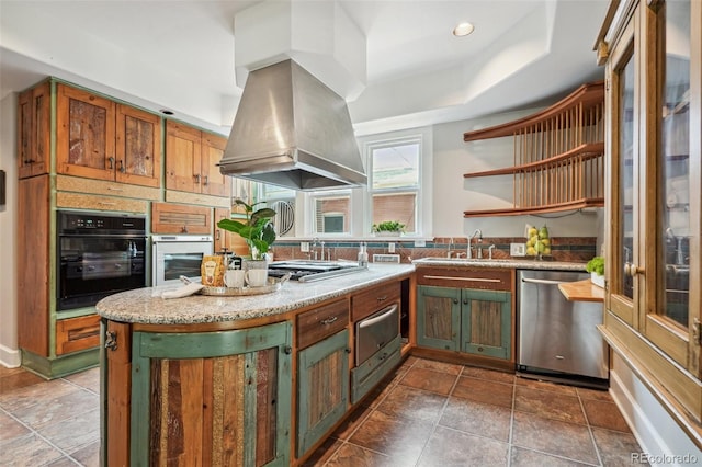 kitchen with appliances with stainless steel finishes, light stone countertops, tile patterned floors, island exhaust hood, and a raised ceiling