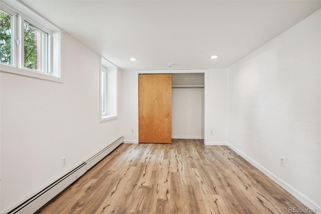 unfurnished bedroom with a closet, a baseboard heating unit, and light wood-type flooring