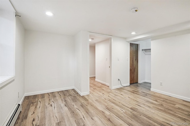 empty room featuring baseboard heating, recessed lighting, light wood-style flooring, and baseboards