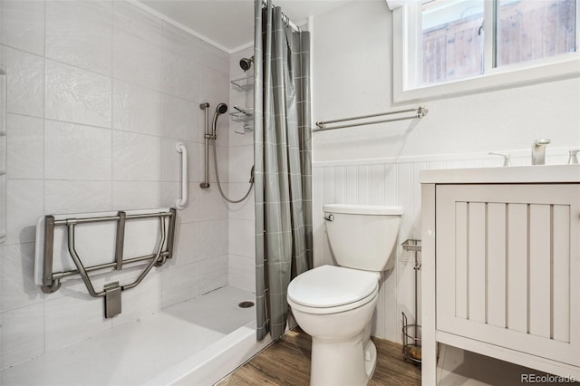 bathroom featuring toilet, a wainscoted wall, wood finished floors, a tile shower, and a sink