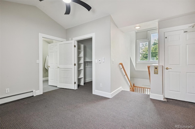 unfurnished bedroom featuring a baseboard radiator, baseboards, vaulted ceiling, dark carpet, and a walk in closet