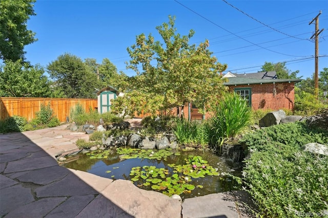 view of yard featuring an outbuilding, a storage shed, fence, a garden pond, and a patio area