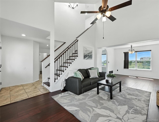 living area featuring a high ceiling, wood finished floors, stairway, arched walkways, and ceiling fan