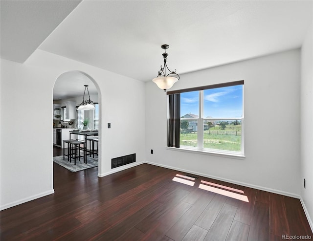empty room with arched walkways and wood finished floors
