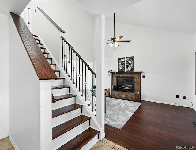 stairs featuring ceiling fan, wood finished floors, a fireplace, and a towering ceiling