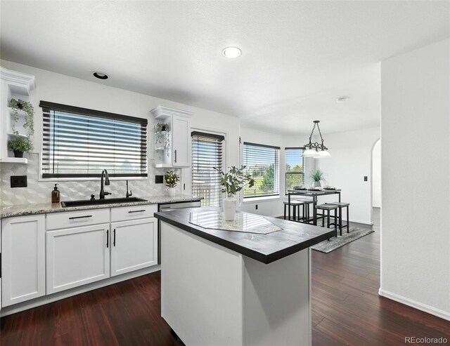 kitchen with decorative backsplash, white cabinets, dark wood-style floors, decorative light fixtures, and a kitchen island