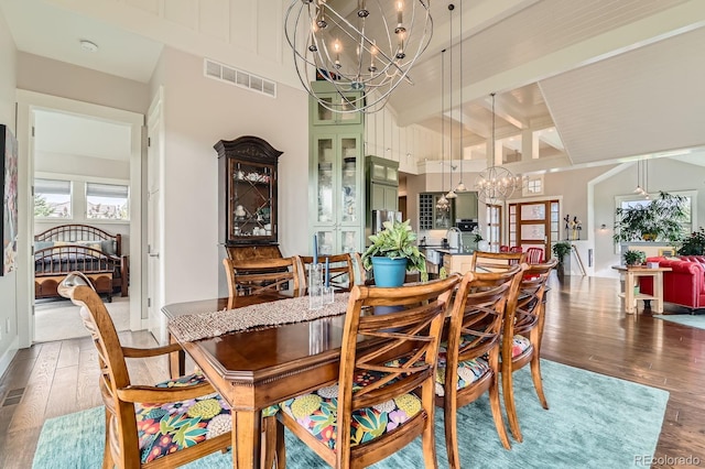 dining space featuring visible vents, beam ceiling, wood finished floors, a chandelier, and a high ceiling