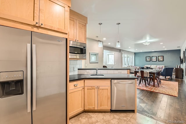 kitchen featuring light brown cabinetry, dark countertops, open floor plan, a sink, and stainless steel appliances