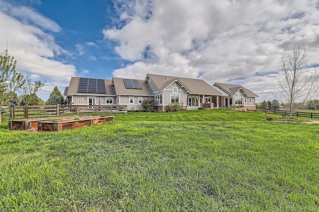 back of property featuring board and batten siding, a vegetable garden, fence, roof mounted solar panels, and a yard
