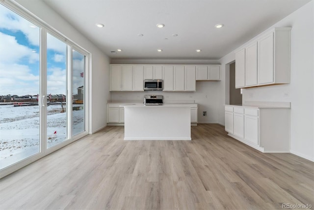 kitchen with stainless steel appliances, white cabinetry, a kitchen island, and light hardwood / wood-style floors