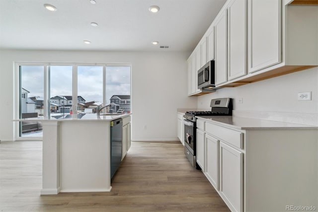 kitchen with a kitchen island with sink, light hardwood / wood-style flooring, white cabinets, and appliances with stainless steel finishes