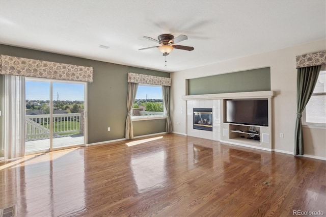 unfurnished living room with a ceiling fan, a tile fireplace, wood finished floors, and baseboards