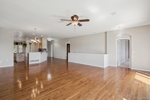 unfurnished living room with arched walkways, a ceiling fan, a chandelier, and wood finished floors