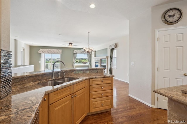 kitchen featuring a sink, stone countertops, dark wood finished floors, decorative light fixtures, and baseboards
