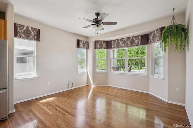 unfurnished room with plenty of natural light, ceiling fan, and wood finished floors