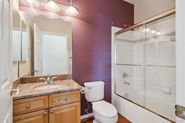 bathroom featuring a textured wall, toilet, vanity, and shower / bath combination with glass door