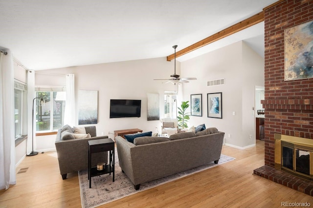 living room featuring vaulted ceiling with beams, visible vents, a brick fireplace, light wood-type flooring, and baseboards