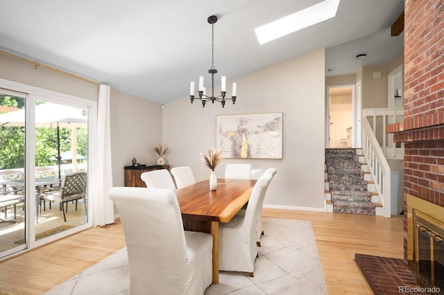 dining room with light wood finished floors, baseboards, lofted ceiling with skylight, stairway, and a chandelier