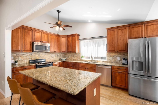 kitchen with a center island, stainless steel appliances, lofted ceiling, brown cabinetry, and a sink