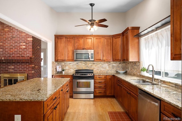 kitchen with stainless steel appliances, brown cabinets, a sink, and light stone counters