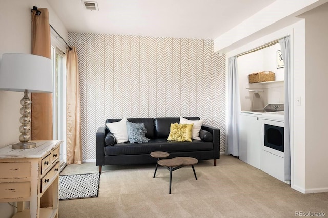 living area with an accent wall, separate washer and dryer, visible vents, and light colored carpet