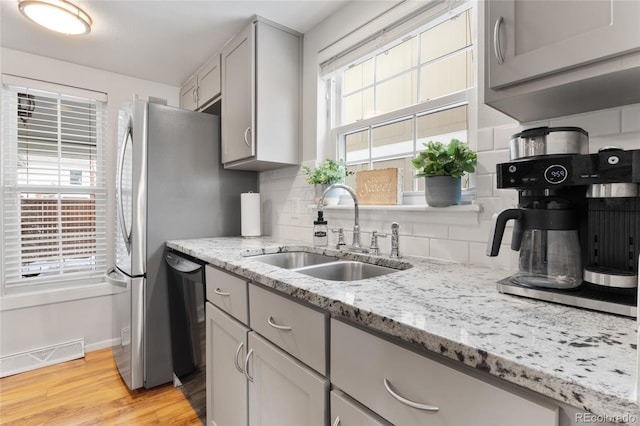 kitchen with light stone counters, light wood-style flooring, decorative backsplash, a sink, and dishwasher