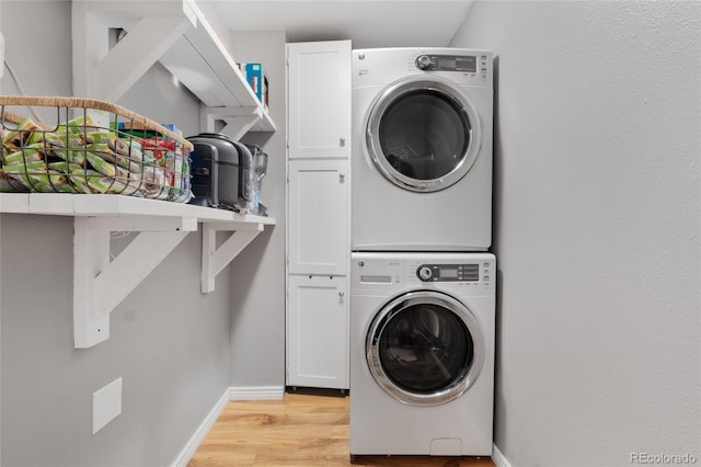 clothes washing area with baseboards, light wood-type flooring, cabinet space, and stacked washer / drying machine