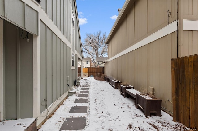 view of snowy exterior with board and batten siding and a fenced backyard