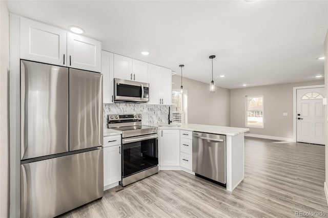 kitchen featuring white cabinets, decorative light fixtures, kitchen peninsula, and appliances with stainless steel finishes