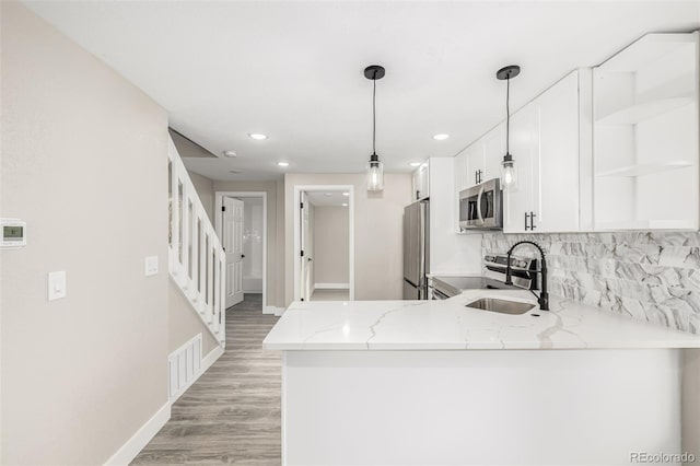 kitchen featuring light stone countertops, kitchen peninsula, pendant lighting, white cabinets, and appliances with stainless steel finishes