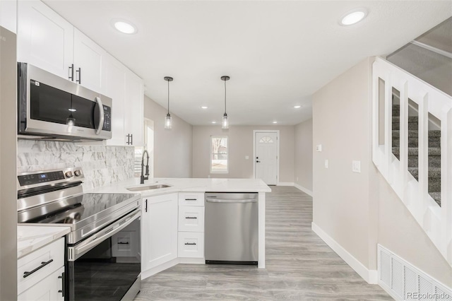 kitchen with appliances with stainless steel finishes, tasteful backsplash, sink, decorative light fixtures, and white cabinets