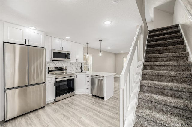 kitchen featuring kitchen peninsula, decorative light fixtures, decorative backsplash, white cabinets, and appliances with stainless steel finishes