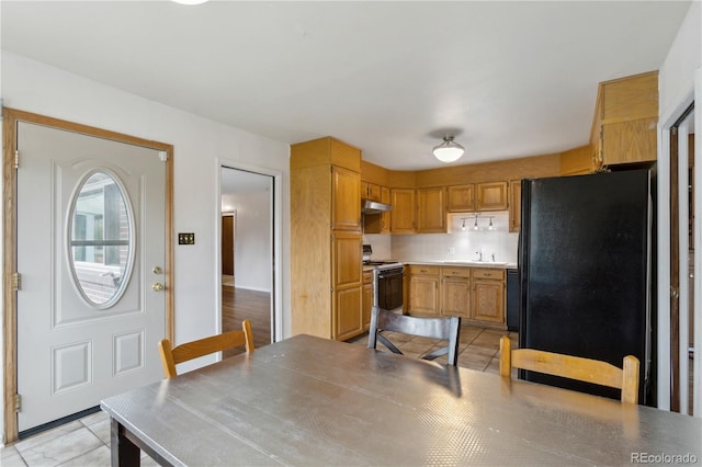 kitchen with black appliances, light tile patterned flooring, under cabinet range hood, a sink, and light countertops