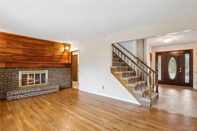 unfurnished living room featuring baseboards, wood finished floors, stairway, and a brick fireplace