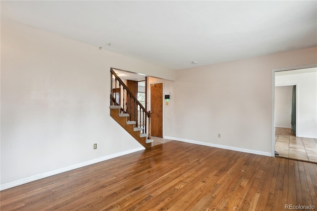 empty room featuring wood-type flooring, stairs, and baseboards