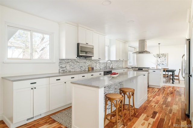 kitchen featuring stainless steel appliances, white cabinetry, range hood, backsplash, and a center island