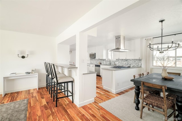 kitchen with range hood, decorative backsplash, appliances with stainless steel finishes, white cabinets, and a peninsula