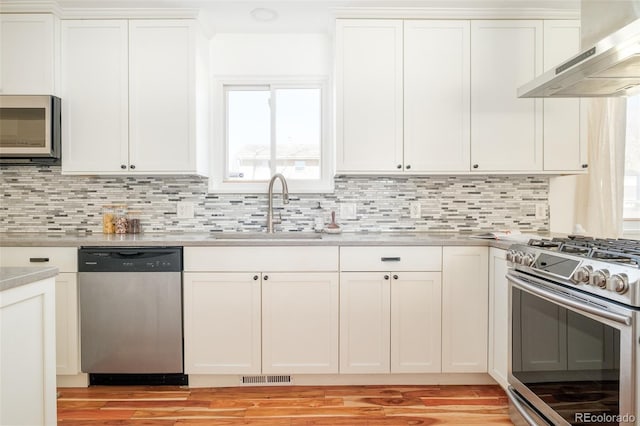 kitchen with visible vents, appliances with stainless steel finishes, white cabinetry, a sink, and wall chimney exhaust hood