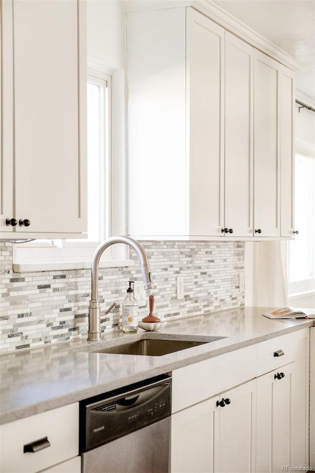 kitchen featuring a sink, white cabinets, stainless steel dishwasher, backsplash, and light stone countertops