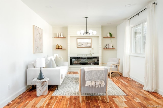 sitting room with baseboards, a glass covered fireplace, wood finished floors, and a notable chandelier