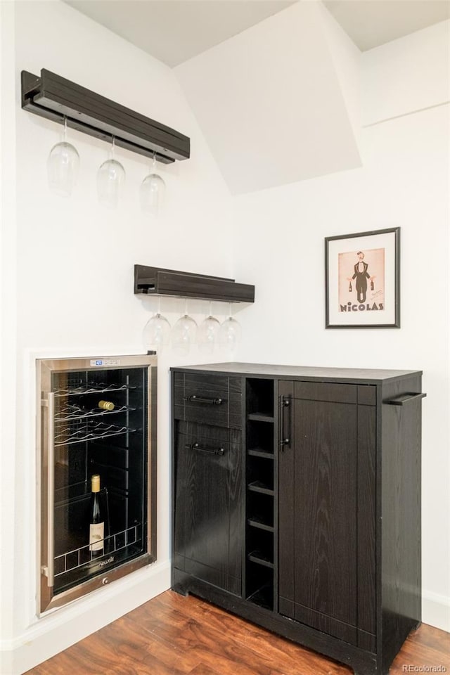 bar featuring lofted ceiling, a bar, wine cooler, and dark wood finished floors