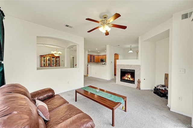 carpeted living room featuring a fireplace and ceiling fan with notable chandelier