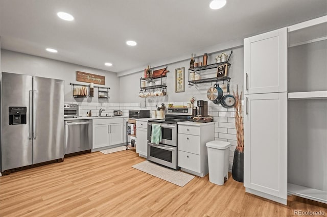kitchen featuring open shelves, light wood-style flooring, stainless steel appliances, light countertops, and white cabinets