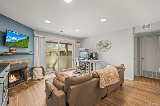 living room featuring a fireplace with flush hearth, wood finished floors, visible vents, and recessed lighting