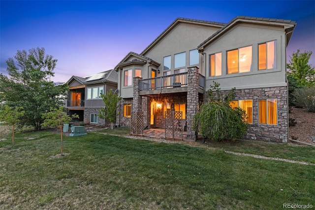 back house at dusk featuring a lawn and a patio