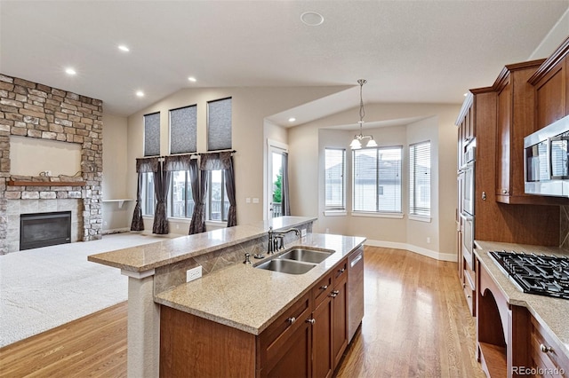 kitchen with decorative light fixtures, stainless steel appliances, sink, light wood-type flooring, and a center island with sink