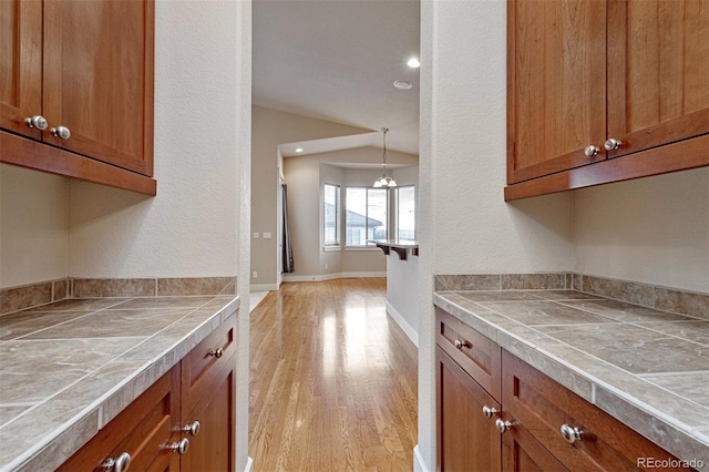 kitchen with vaulted ceiling, tile countertops, light hardwood / wood-style floors, and decorative light fixtures