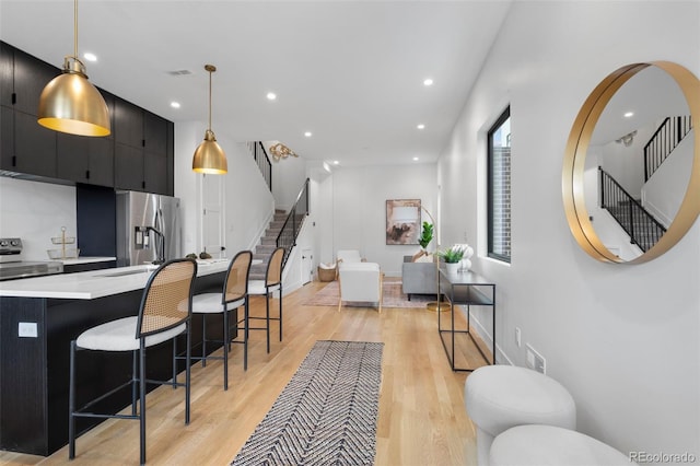 kitchen with stainless steel appliances, a kitchen breakfast bar, light countertops, dark cabinetry, and light wood-type flooring