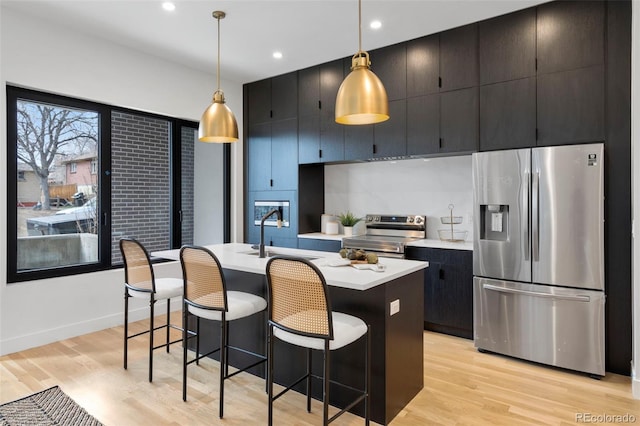 kitchen featuring a center island with sink, appliances with stainless steel finishes, light countertops, light wood-type flooring, and a sink